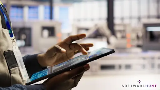 Close‑up of a factory worker using a tablet on the shop floor to track production and inventory data in real time, with blurred industrial machines behind